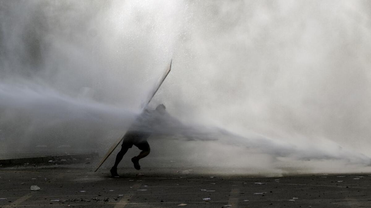 A demonstrator is hit by a riot police water cannon spray during a protest against the government in Santiago on November 18, 2019. President Sebastian Pinera condemned on Sunday for the first time what he called abuses committed by police in dealing with four weeks of violent unrest that have rocked Chile and which has left 22 people dead and more than 2,000 injured. Chileans have been protesting social and economic inequality, and against an entrenched political elite that comes from a small number of the