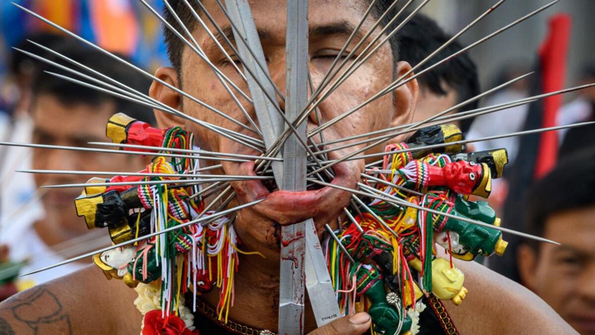 AFP PICTURES OF THE YEAR 2019 - A devotee of a Chinese shrine with multiple skewers pierced through his cheeks takes part in a procession during the annual Vegetarian Festival in Phuket on October 3, 2019. The festival begins on the first evening of the ninth lunar month and lasts for nine days, with many religious devotees slashing themselves with swords, piercing their cheeks with sharp objects and committing other painful acts to purify themselves, taking on the sins of the community. Mladen ANTONOV / AF