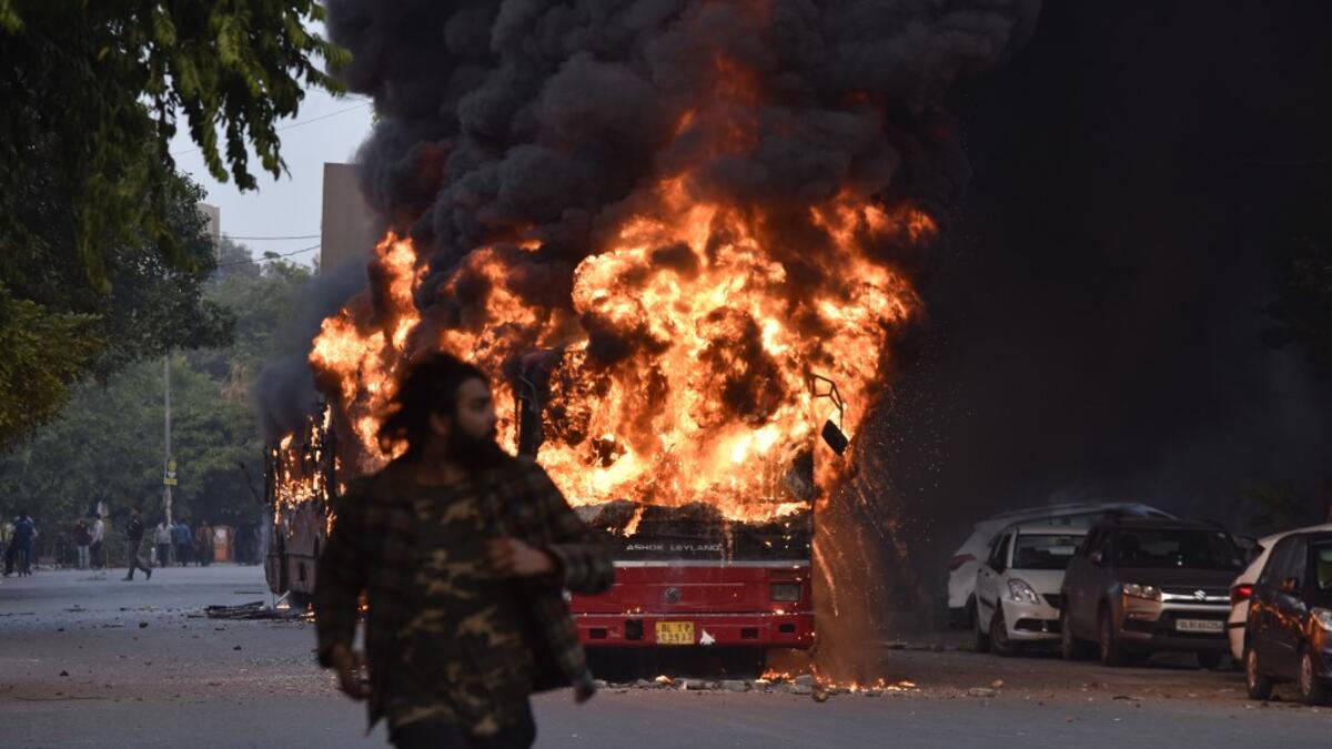 A man walks on a street as a bus is on fire following a demonstration against the Indian government's Citizenship Amendment Bill (CAB) in New Delhi on December 15, 2019. Angry protesters in northeast India vowed on December 15 to keep demonstrating against a contentious citizenship law as the death toll from bloody clashes opposing the bill rose to six. STR / AFP