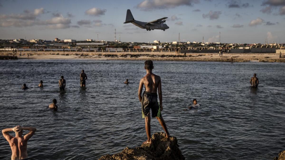 Soldiers enjoying a day off and Somali people look from the beach at a military plane landing within Mogadishu’s airport base in Mogadishu, Somalia, on December 13, 2019. LUIS TATO / AFP