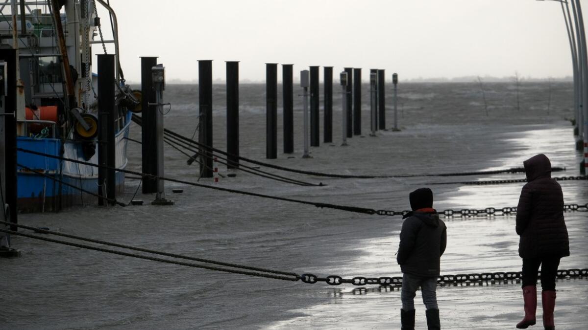 People walk near fish trawlers at the flooded harbor of Wremen, on the North Sea near Bremerhaven, northern Germany, on Febuary 11, 2020. Fierce winds and heavy rains claimed at least six lives across northern Europe on February 11, 2020, as Storm Ciara disrupted travel, grounded hundreds of flights, flooded roads and left vast areas without power. Patrik Stollarz / AFP