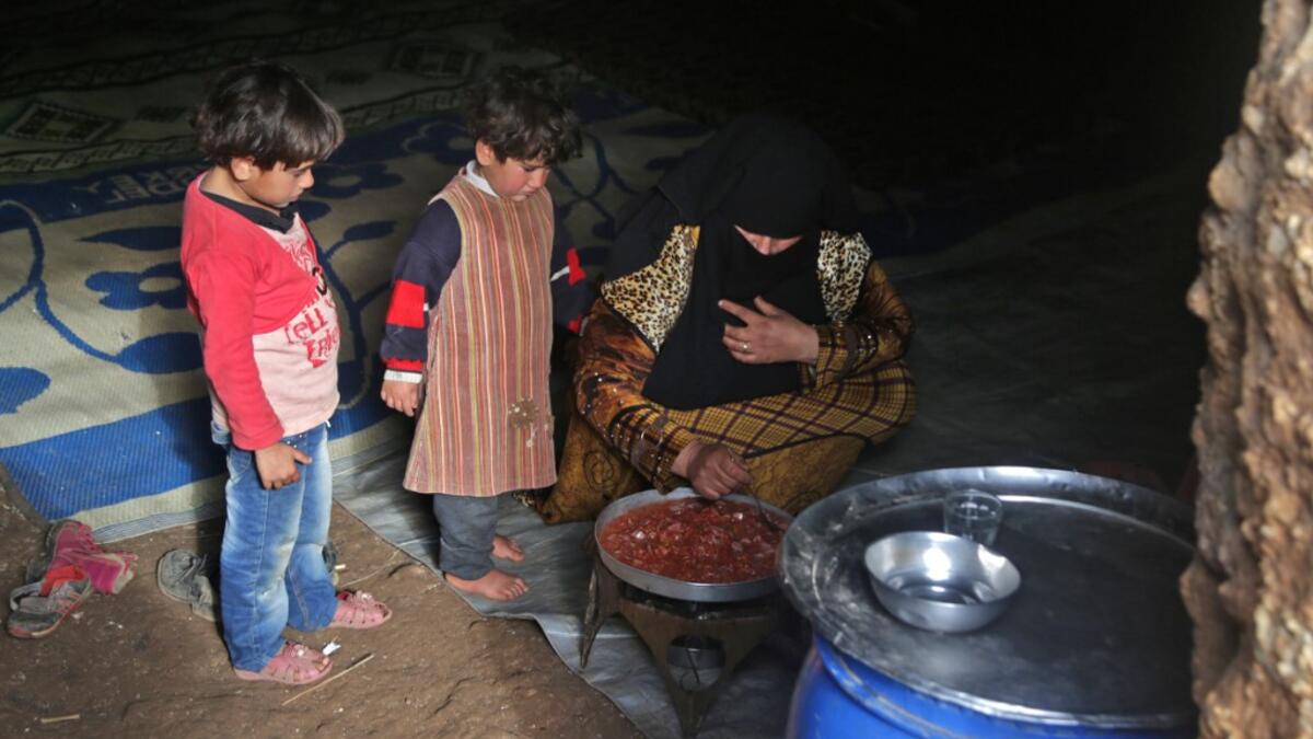 Children stand by a woman preparing food inside an underground shelter where several families of internally displaced Syrians from Aleppo and Idlib provinces are taking refuge, in the village of Taltunah about 15 kilometres northwest of Idlib in the northwestern Idlib province, on February 23, 2020. Aref TAMMAWI / AFP