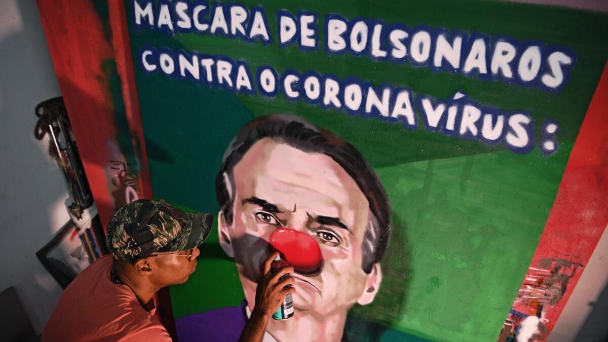 Brazilian graffiti artist Aira Ocrespo finishes an art piece featuring Brazil's President Jair Bolsonaro reading "Bolsonaro's mask against the Coronavirus" at his studio in Rio de Janeiro, Brazil, on March 18, 2020. Bolsonaro gave a press conference today wearing a facemask as he spoke about the COVID-19 coronavirus pandemic. CARL DE SOUZA / AFP