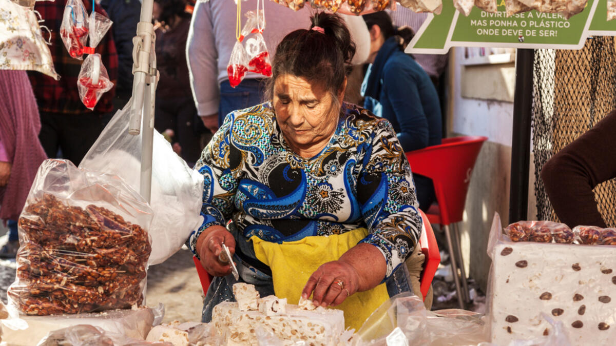 Elderly woman chops blocks of nougat at a market in Portugal (Shutterstock)