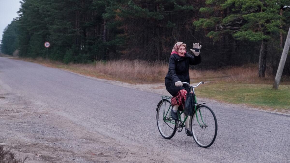 An elderly woman on her bicycle waves on November 20, 2019 on Kihnu island in the Baltic Sea, 10 kilometres (six miles) off the coast of Estonia. Steeped in folk traditions, Kihnu's historic way of life however is now threatened as economic hardship drives more and more islanders away in search of work. Alessandro RAMPAZZO / AFP