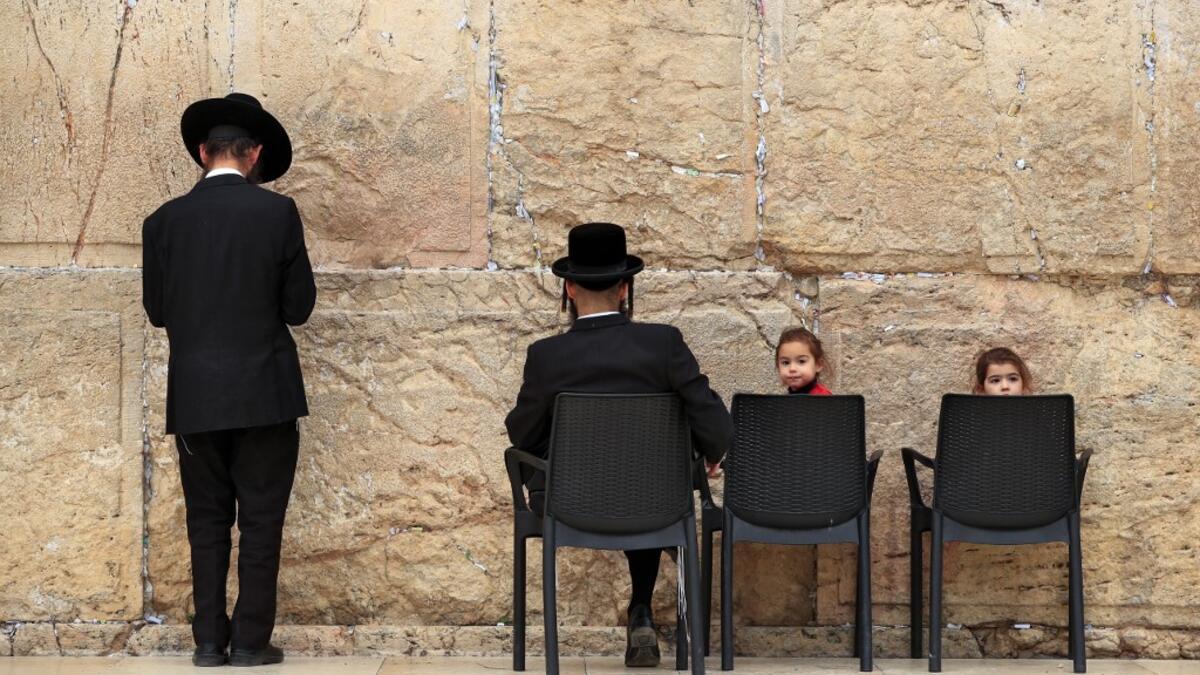 Children sit in chairs next to ultra-Orthodox Jewish men praying at the nearly deserted Western Wall, the holiest site where Jews can pray, after Israel has imposed some of the world's tightest restrictions to contain COVID-19 coronavirus disease, in Jerusalem on March 12, 2020. Israel imposed a two-week quarantine on all travellers entering the country, almost stopping tourism and limiting public gatherings as officials confirmed its 100th case of the COVID-19 coronavirus disease. Emmanuel DUNAND / AFP
