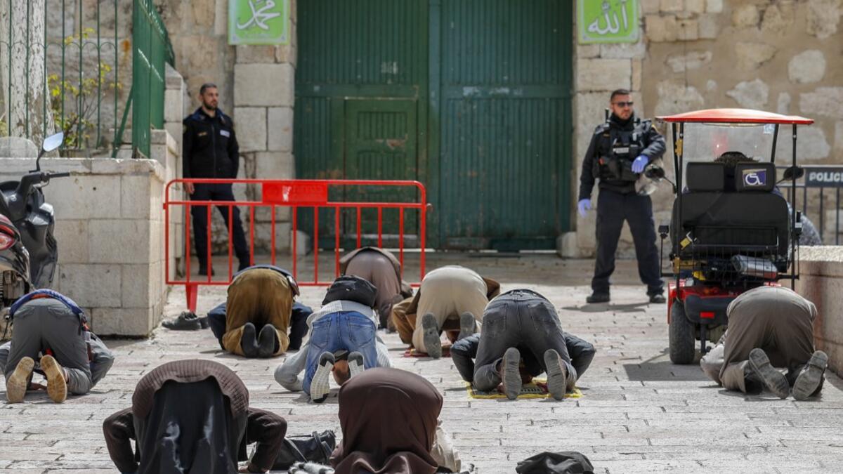 This picture taken on March 23, 2020 shows Palestinian Muslim men prostrate in prayer as Israeli security forces watch near the closed gate of the Aqsa mosque compound, which was closed by the Jordan Waqf religious authority administering the site as part of preventive measures against the spread of the COVID-19 novel coronavirus, in Jerusalem. Over a 24-hour period, in a world where a third of humanity is now under orders to stay home, AFP photographers have captured snapshots of daily life during the coro