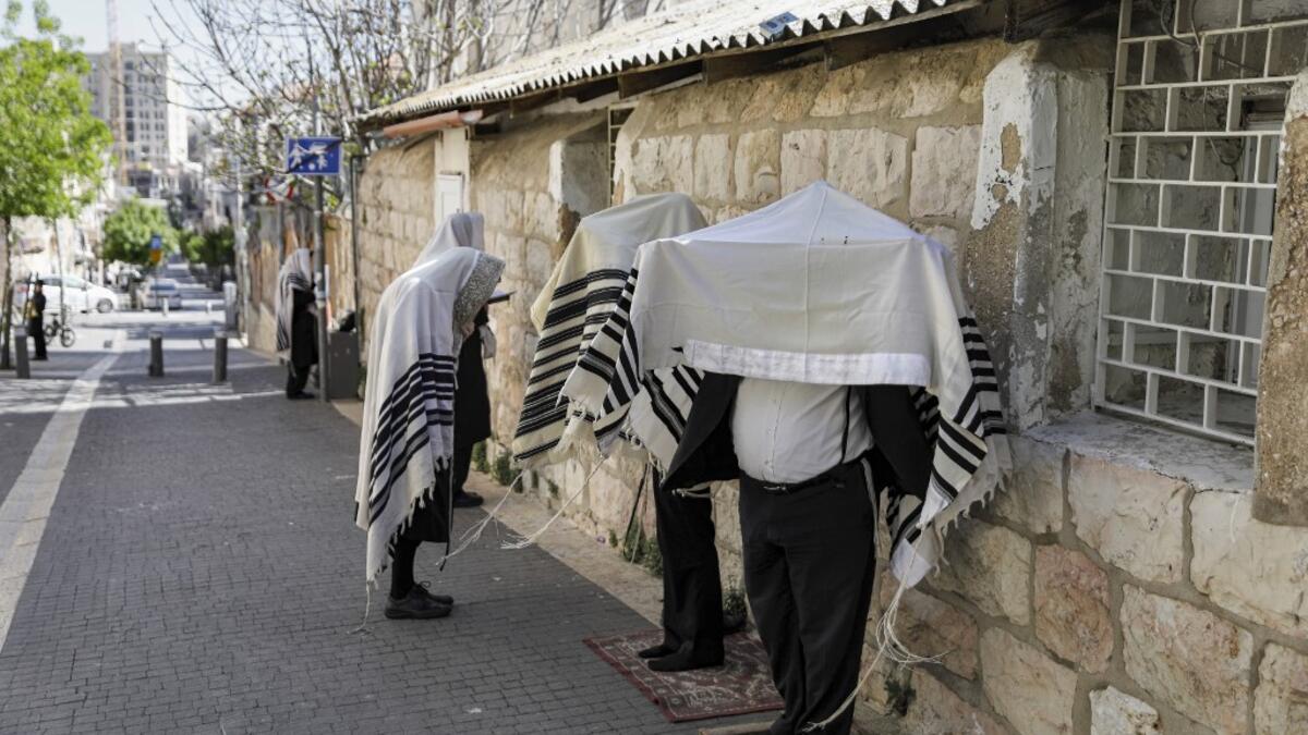 Ultra-Orthodox Jews, wearing the traditional Tallit Jewish prayer shawls, pray along a street outside their closed synagogue in Jerusalem on March 29, 2020, while keeping a distance of two metres from one another following instructions to stop the spread of the COVID-19 coronavirus pandemic. MENAHEM KAHANA / AFP