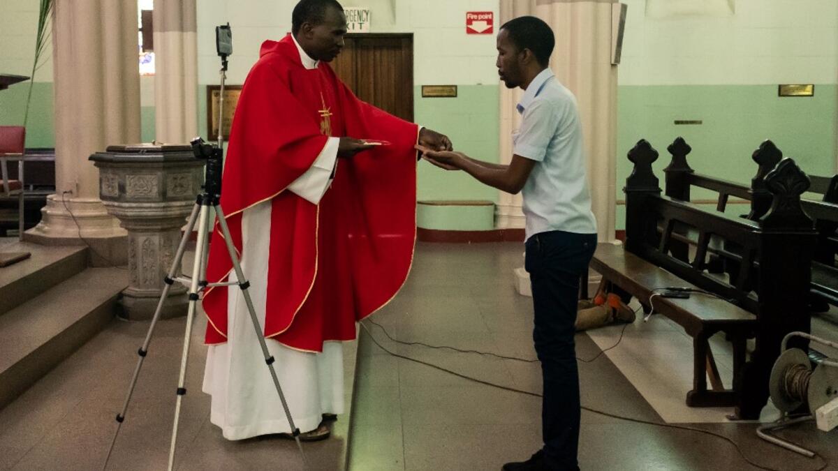 Father Kennedy Mugute, the Vicar General of the Archdiocese of Harare, gives communion to the head of media Ronald Mapfumo (R), as he conducts a Palm Sunday mass, which is livestreamed to parishioners on Facebook, in the empty Cathedral of the Sacred Heart in Harare, on April 5, 2020, on the seventh day of a lockdown in Zimbabwe. AFP