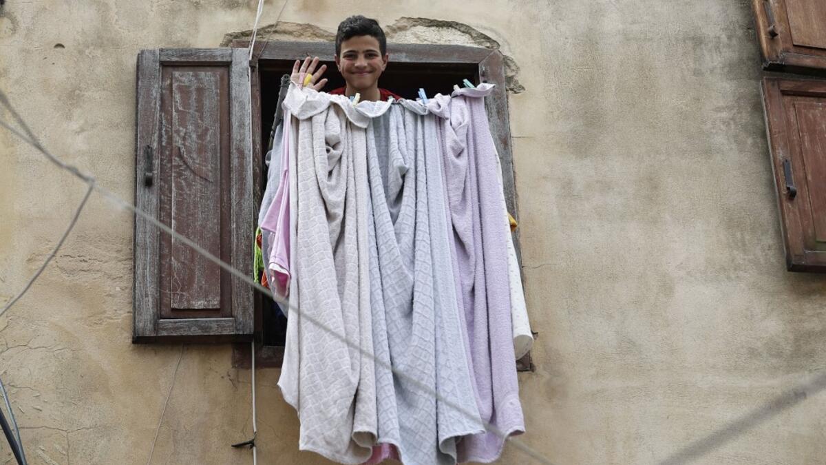 A Lebanese youth waves in greeting as he looks out of a window during confinement at home due to the COVID-19 pandemic, in the historic part of the southern coastal city of Sidon (Saida), on April 6, 2020. Lebanon's President called on international donors to provide financial assistance to the crisis-hit country as it grapples with a severe economic downturn compounded by the novel coronavirus pandemic. JOSEPH EID / AFP