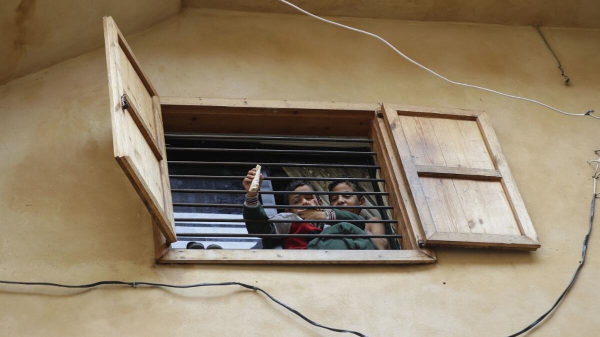 Lebanese youths sit at a barred window during confinement at home due to the COVID-19 pandemic, in the historic part of the southern coastal city of Sidon (Saida), on April 6, 2020. Lebanon's President called on international donors to provide financial assistance to the crisis-hit country as it grapples with a severe economic downturn compounded by the novel coronavirus pandemic. JOSEPH EID / AFP