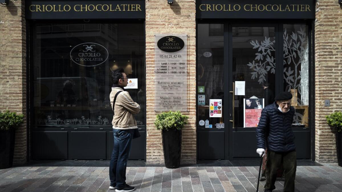 A client leaves Criollo chocolate maker shop after buying Easter chocolates as another one waits outside to respect the rules of social distancing in shops on April 7, 2020 in Toulouse, southern France, on the twenty-second day of a strict lockdown in France to stop the spread of COVID-19, caused by the novel coronavirus. Lionel BONAVENTURE / AFP
