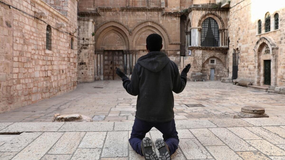 A Christian worshipper kneels in prayer facing the shut doors of the Church of the Holy Sepulchre in Jerusalem's Old City on April 7, 2020, amid the COVID-19 pandemic. All cultural sites in the Holy Land are shuttered, regardless of their religious affiliation, as authorities seek to forestall the spread of the deadly respiratory disease, which will prevent Christians from congregating for the Easter service, this coming Sunday for Catholic worshippers, then a week later on April 19 for Orthodox Easter. GAL
