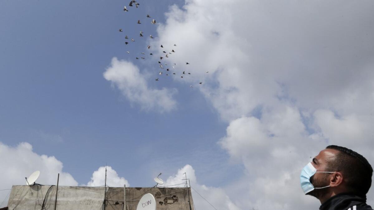 A pigeon owner, wearing personal protective equipment, watches his pigeons fly on the rooftop of his building in the southern suburb of Beirut on April 11, 2020. ANWAR AMRO / AFP