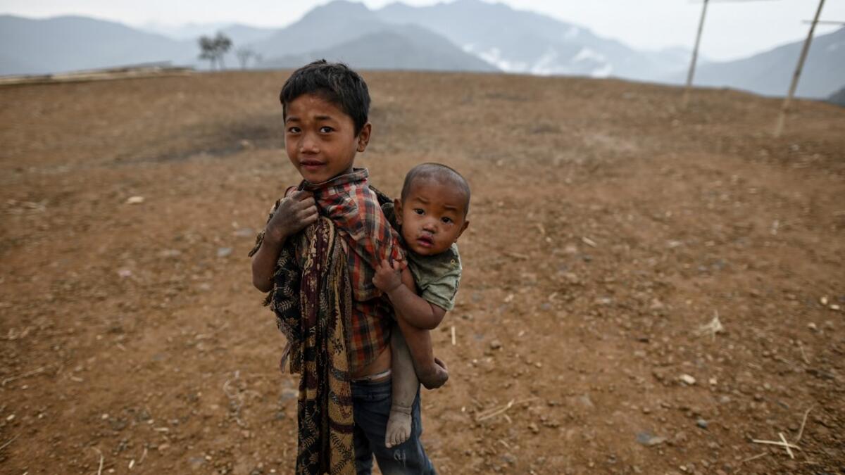 This photo taken on February 9, 2020 shows a boy carrying his brother in front of their house in Karmawlawyi village in Myanmar's Sagaing region, near the border with India. The king of the Konyak tribe sleeps in Myanmar, but eats in India -- his house, village and people divided by a mountain border which serves as a vulnerable lifeline now severed by a coronavirus lockdown.  Ye Aung THU / AFP