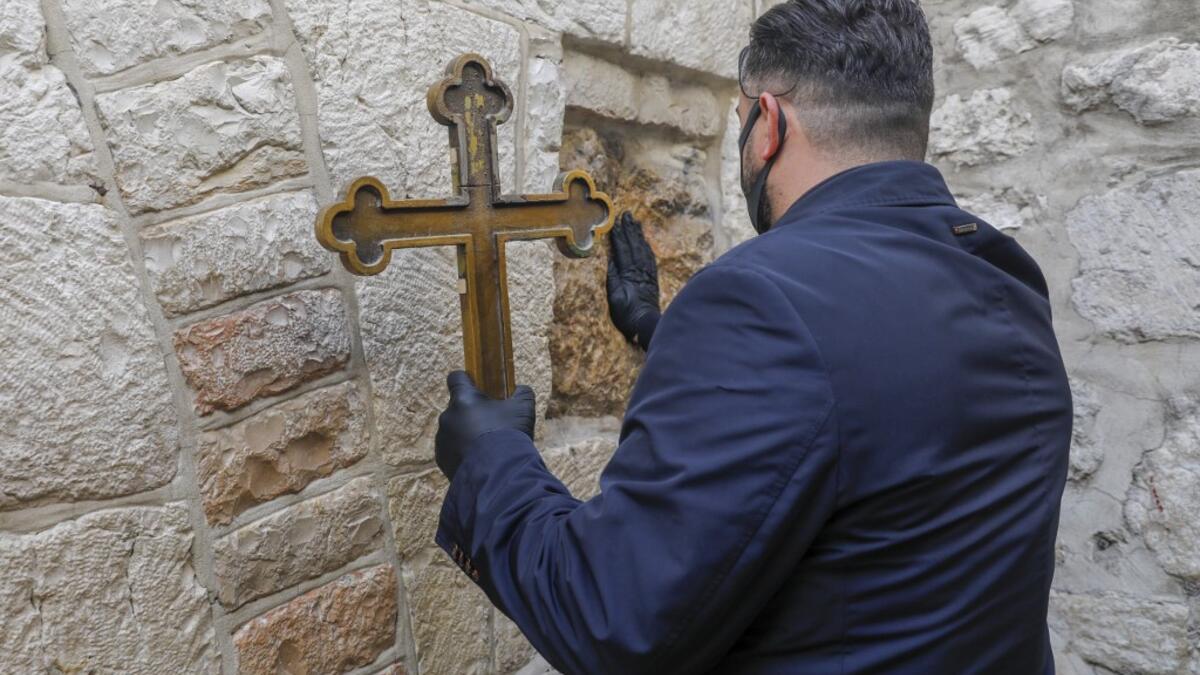 A Christian worshipper wearing a face mask, due to the COVID-19 coronavirus pandemic, touches one of the stations of the Via Dolorosa (Way of Sorrow), the path traditionally believed to have been taken by Christ while on the way to be crucified, to receive a blessing, in the old city of Jerusalem on Orthodox Holy Friday April 17, 2020. AHMAD GHARABLI / AFP