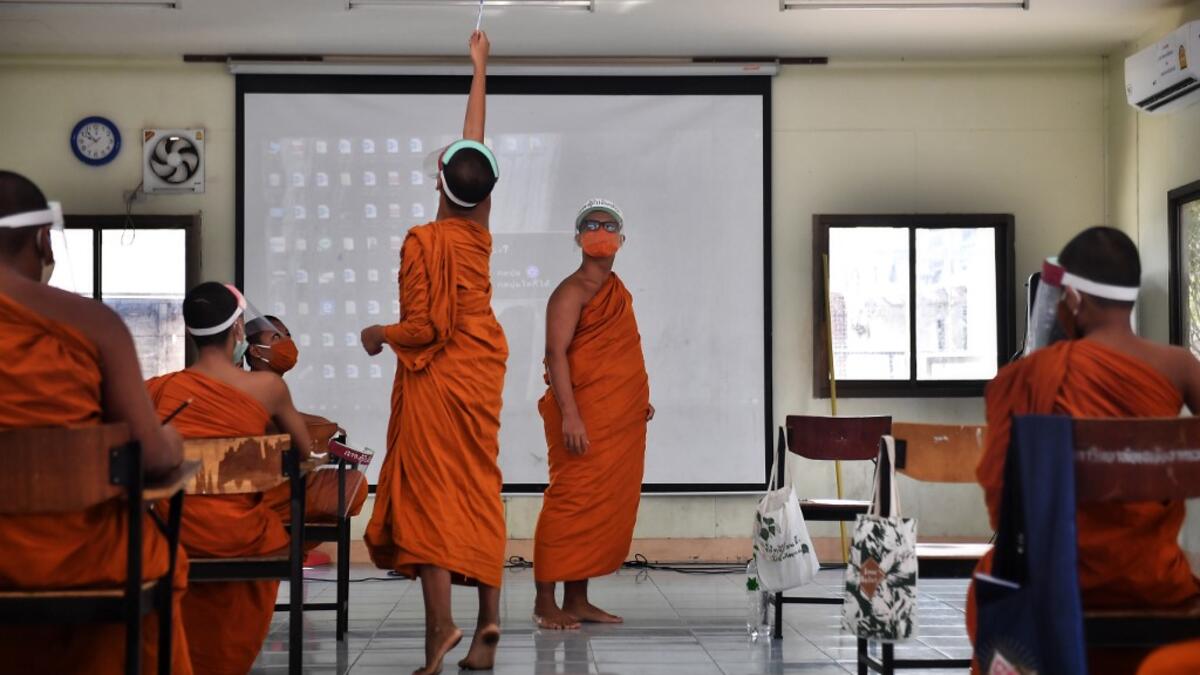 A novice monk wearing a face shield as a preventive measure against the spread of the COVID-19 coronavirus turns off a projector during religious studies at Wat Molilokkayaram Buddhist temple in Bangkok on April 20, 2020. Lillian SUWANRUMPHA / AFP