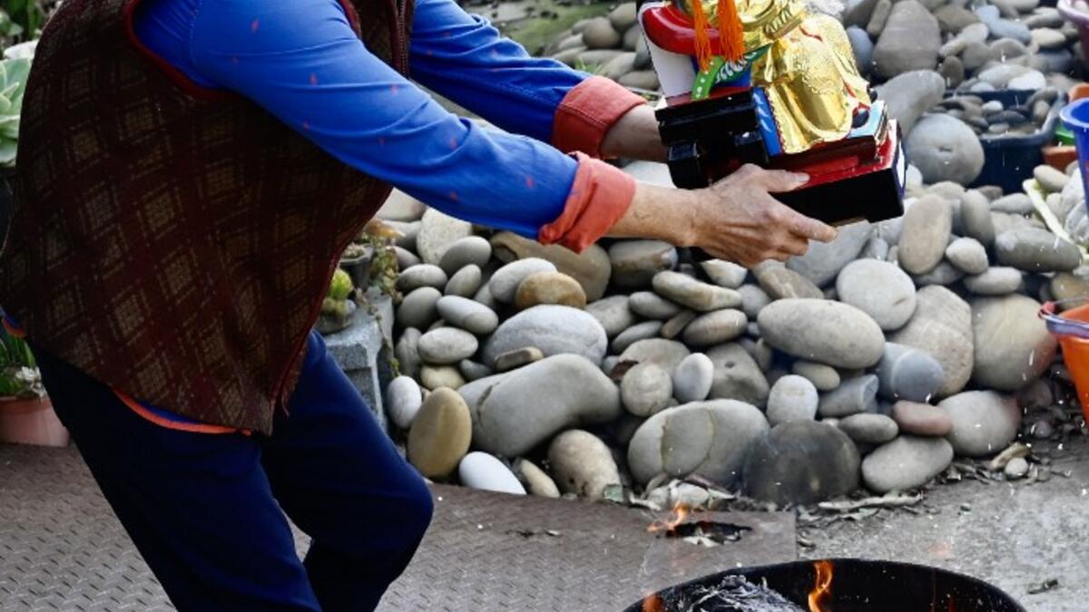 In this picture taken on March 17, 2020, a woman holds her new Taoist god statue above a fire during a blessing ceremony after it was restored by sculptor Lin Hsin-lai at his workplace in Taoyuan, northern Taiwan. Every spare surface of Lin Hsin-lai's four-storey shop is crammed with a pantheon of Taiwan's celestial beings, testament to the decades he has spent sheltering and restoring unwanted statues of gods.  Sam Yeh / AFP