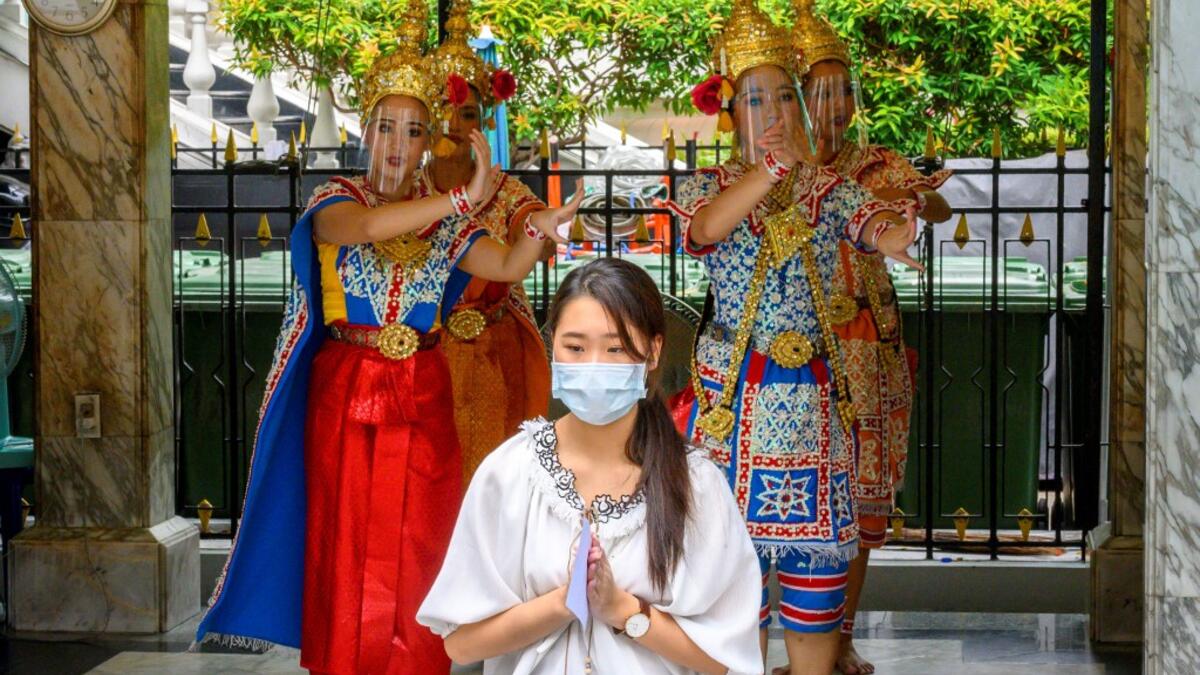 Traditional Thai dancers wearing protective face shields perform behind a woman praying at the Erawan Shrine, which was reopened after the Thai government relaxed measures to combat the spread of the COVID-19 novel coronavirus, in Bangkok on May 4, 2020. Thailand began easing restrictions related to the COVID-19 novel coronavirus on May 3 by allowing various businesses to reopen, but warned that the stricter measures would be re-imposed should cases increase again. Mladen ANTONOV / AFP