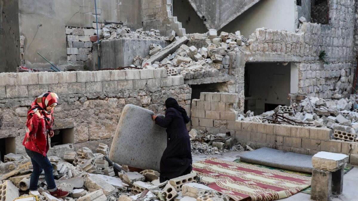 This picture taken on May 4, 2020 during the Muslim holy fasting month of Ramadan shows the mother of Tareq Abu Ziad (L), a displaced Syrian from the town of Ariha in the southern countryside of the Idlib province, preparing to put up a mattress so members of her family can sit to break their fast together for the sunset "iftar" meal, in the midst of the rubble of their destroyed home upon their return to the town for one day after fleeing during the previous military assault by Syrian government forces and
