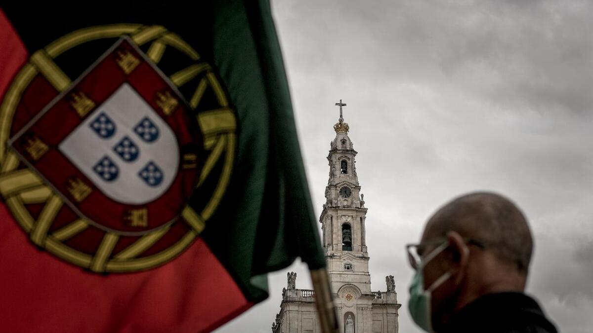 A man holds a Portuguese flag during the 103rd anniversary of the apparitions of Our Lady of Fatima at the Fatima shrine in central Portugal on May 13, 2020. Without the crowd of pilgrims it welcomes every year, the shrine of Fatima celebrated the anniversary during a religious ceremony reduced to the bare minimum. PATRICIA DE MELO MOREIRA / AFP
