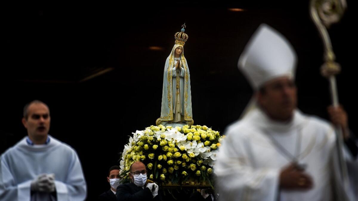 The statue of Our Lady Fatima is carried by people wearing face masks during the 103rd anniversary of the apparitions of Our Lady Fatima at the Fatima shrine in central Portugal on May 13, 2020. Without the crowd of pilgrims it welcomes every year, the shrine of Fatima celebrated the anniversary during a religious ceremony reduced to the bare minimum. PATRICIA DE MELO MOREIRA / AFP