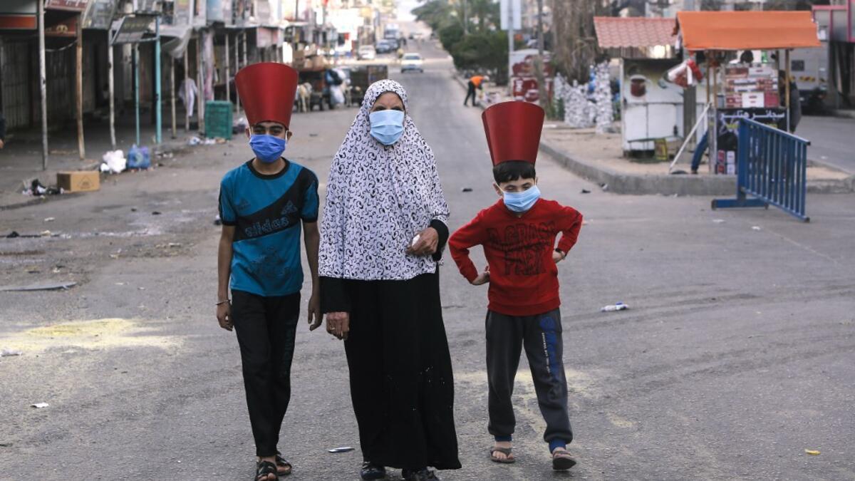 A Palestinian woman and paper-hat-clad children, wearing masks due to the COVID-19 coronavirus pandemic, walk along a street in Gaza City early on May 24, 2020, after performing prayers on the first day of Eid al-Fitr, the Muslim holiday which starts at the conclusion of the holy fasting month of Ramadan. Local authorities in the Hamas-run Palestinian enclave allowed mosques to reopen for Eid al-Fitr as social distancing procedures for the novel coronavirus are maintained while encouraging the elderly to pe