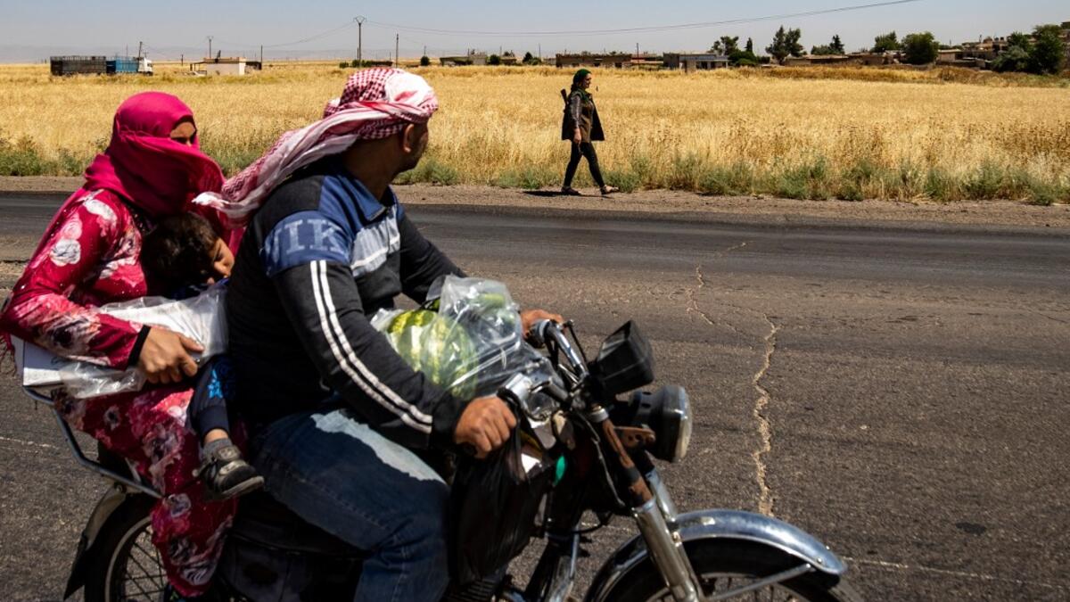 A family rider a motorcycle past a Kurdish female volunteer, from the newly formed Community Protection Forces, as she patrols a wheat field, against threats by jihadists to burn the crops, during harvest season on June 13, 2020, in the countryside east of Qamishli in Syria's northeastern Hasakah province. Delil SOULEIMAN / AFP