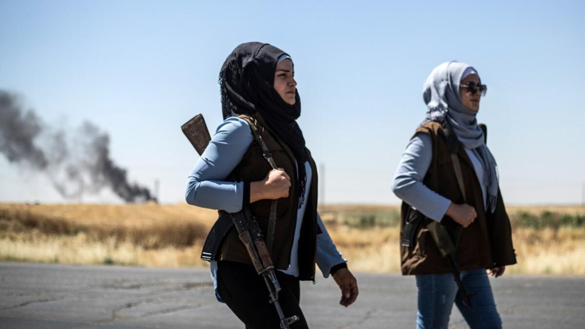 Smoke billows from an oil field as Kurdish female volunteers, from the newly formed Community Protection Forces, guard a wheat field, against threats by jihadists to burn the crops, during harvest season on June 13, 2020, in the countryside east of Qamishli in Syria's northeastern Hasakah province. Delil SOULEIMAN / AFP