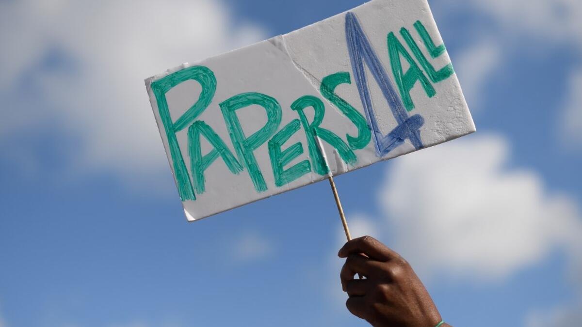 A woman holds a placard reading "Papers for all" during a migrant´s demonstration in Barcelona on June 20, 2020, marking World Refugee Day and demanding legal papers for refugees and migrants in Spain. Josep LAGO / AFP