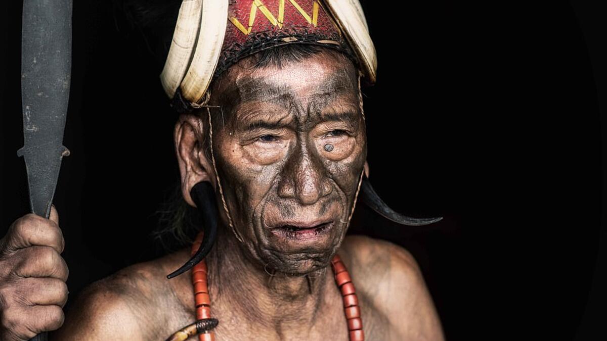 A shirtless tribesman warrior is pictured wearing a traditional headdress and brandishing a spear with a heavily tattooed chest.  (Mediadrumimages/ Trevor Cole)