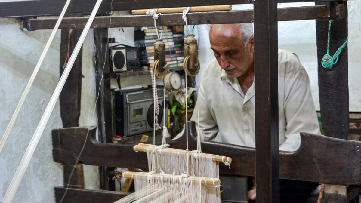 Muhammad Saud, a 65-year-old Syrian silk farmer, handweaves silk threads on a loom at his home workshop in the village of Deir Mama, in west-central Syria on June 22, 2020. MAHER AL MOUNES / AFP