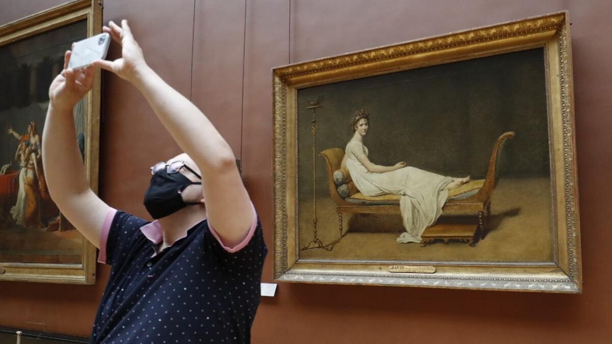 A woman wearing face mask takes a pictures as she visit the Louvre Museum in Paris on July 6, 2020, on the museum' s reopening day. FRANCOIS GUILLOT / AFP