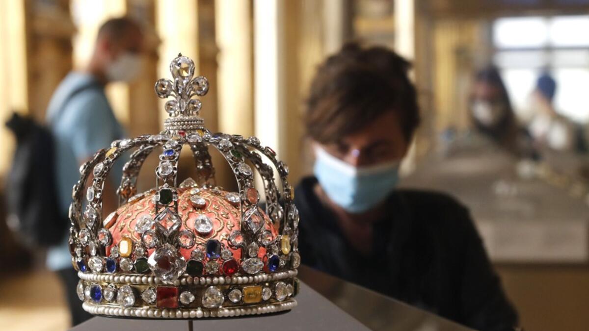 A visitor wearing face mask stands in front of the Crown of Louis XV held in the Apollo gallery at the Louvre Museum in Paris on July 6, 2020, on the museum' s reopening day. FRANCOIS GUILLOT / AFP