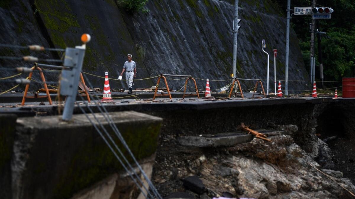 A man walks along a road damaged from recent heavy rains and flooding in the village of Kuma, Kumamoto prefecture on July 9, 2020. Japanese emergency services and troops were scrambling on July 9 to reach thousands of homes cut off by catastrophic flooding and landslides that have killed dozens and caused widespread damage. CHARLY TRIBALLEAU / AFP