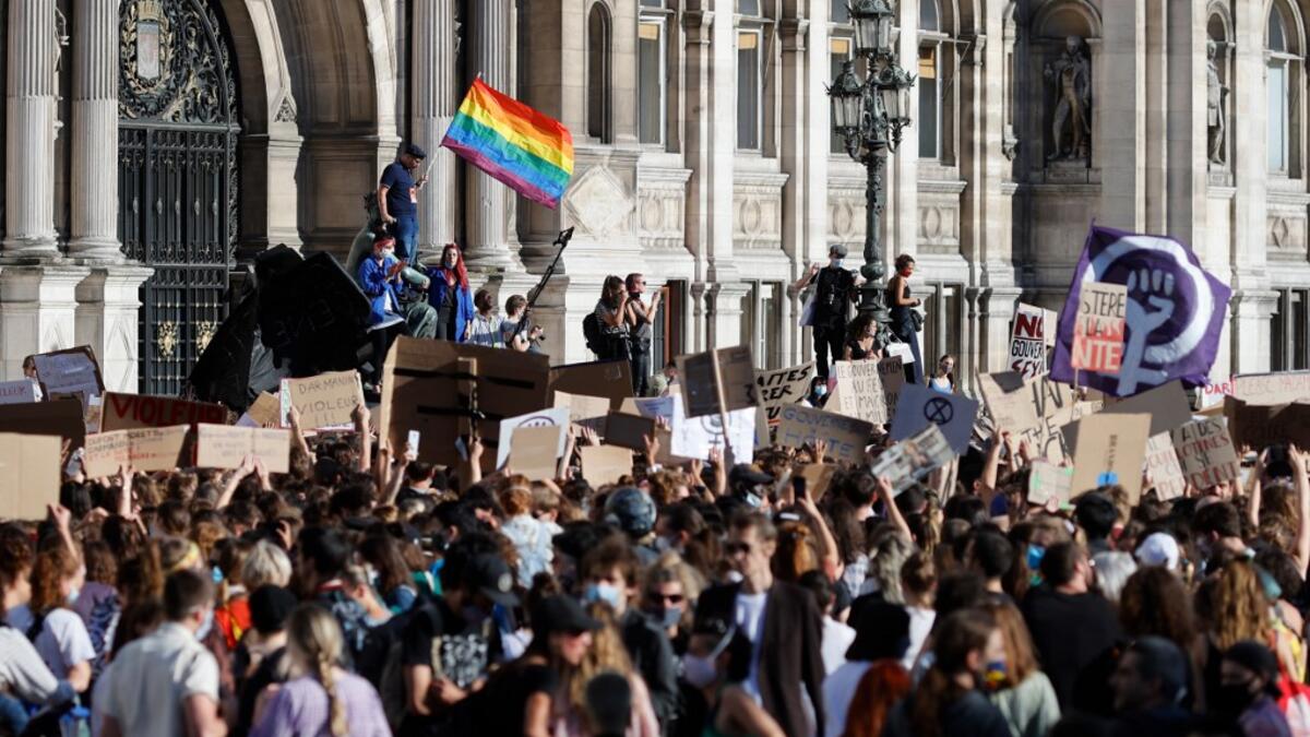 A protester (L) waves a rainbow flag, symbol of LGBTQ social movements, and others hold placards during a demonstration called by feminist movements in front of the city hall in Paris, on July 10, 2020, to denounce the nomination of French Interior Minister, facing rape accusations and French Justice Minister who criticised the #MeToo movement against sexual harassment. Thomas COEX / AFP