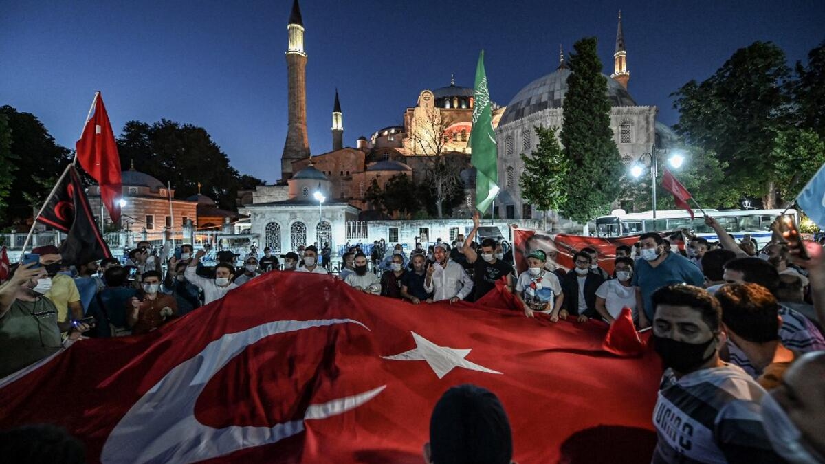 People, some wearing face masks, wave a giant Turkey national flag and shout slogans outside the Hagia Sophia museum in Istanbul on July 10, 2020 as they gather to celebrate after a top Turkish court revoked the sixth-century Hagia Sophia's status as a museum, clearing the way for it to be turned back into a mosque. The Council of State, the country's highest administrative court which on July 2 debated a case brought by a Turkish NGO, cancelled a 1934 cabinet decision and ruled the UNESCO World Heritage si
