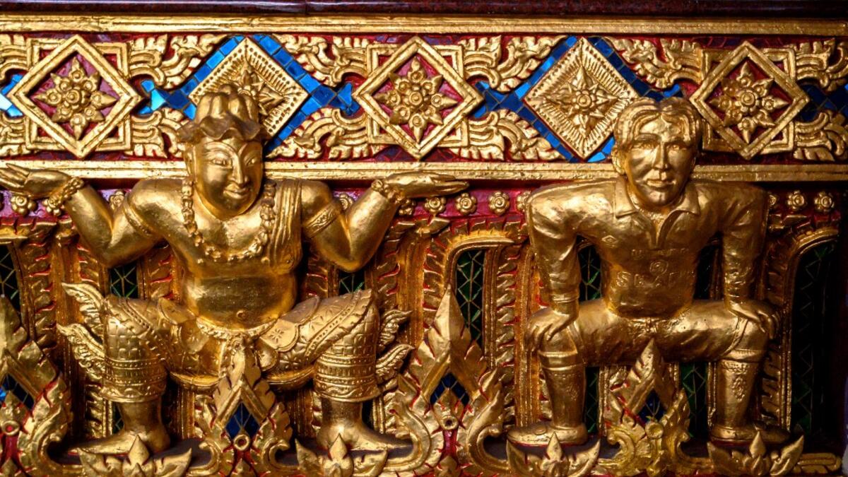 This photograph taken on July 14, 2020 shows a gold-plated sculpture of British football player David Beckham (R) in a Manchester United jersey at the base of a Buddha statue at the Wat Pariwat Buddhist temple in Bangkok. Wat Pariwat, also known as "the David Beckham Temple", is decorated with statues of superheroes and comic characters as well as mythical and imaginary creatures. A golden-plated sculpture of the English football player holding the base of a Buddha statue in one of the buildings gives the t