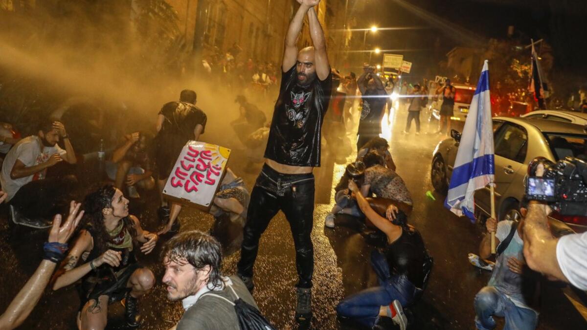 A protester holds up his fists as Israeli police spray the crowd with water cannon during a rally against Prime Minister Benjamin Netanyahu in Jerusalem, on July 19, 2020 amid the coronavirus pandemic. Israeli police fired water cannons to disperse anti-government protests attended by thousands on Saturday, as public anger mounts over the handling of the coronavirus crisis.