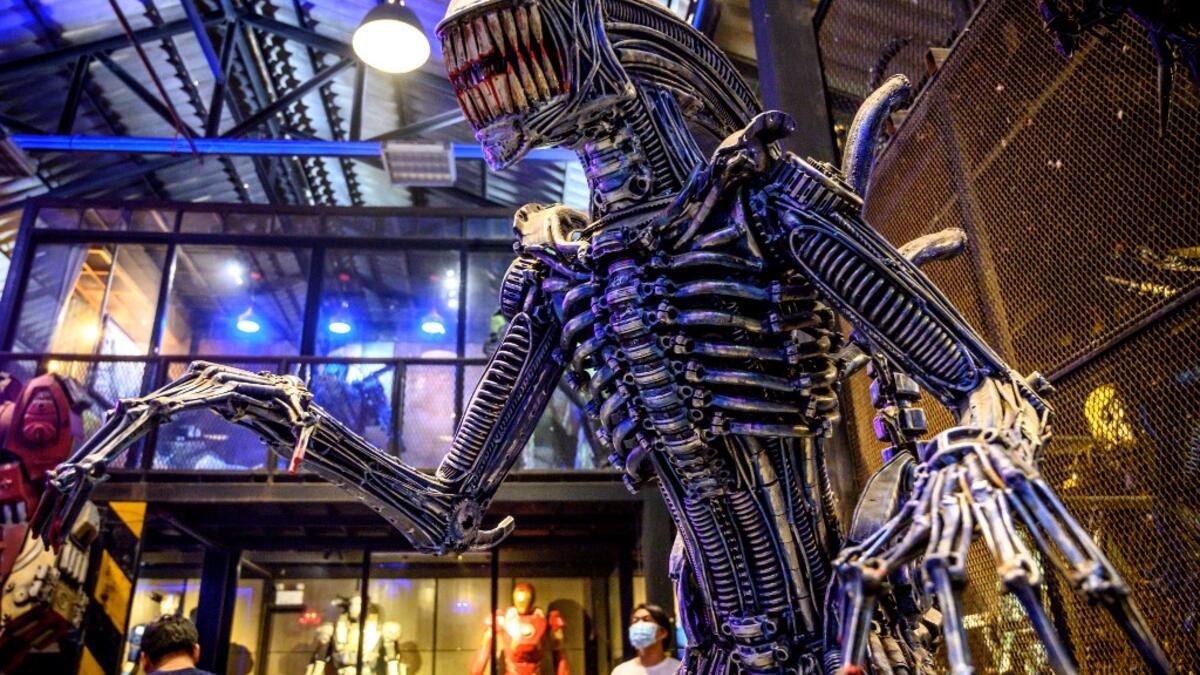 This photograph taken on July 18, 2020 shows tourists looking at a life-sized sculpture of a character from the "Alien" film series made of scrap metal parts at the Ban Hun Lek museum in Ang Thong, some 100km north of Bangkok. "Ban Hun Lek" or "The House of Steel Robots" is a museum where a collective of artists display their scrap metal creations depicting popular comics and sci-fi film characters. Mladen ANTONOV / AFP