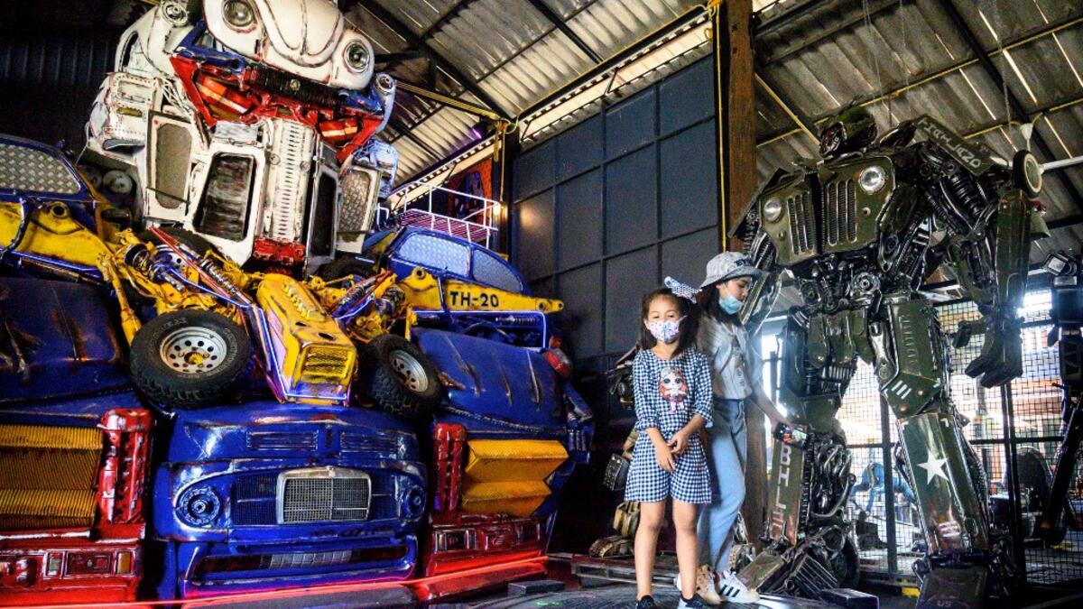 This photograph taken on July 18, 2020 shows children playing in front of a life-sized sculpture of a character from the "Transformers" film franchise made of scrap metal parts at the Ban Hun Lek museum in Ang Thong, some 100km north of Bangkok. "Ban Hun Lek" or "The House of Steel Robots" is a museum where a collective of artists display their scrap metal creations depicting popular comics and sci-fi film characters. Mladen ANTONOV / AFP