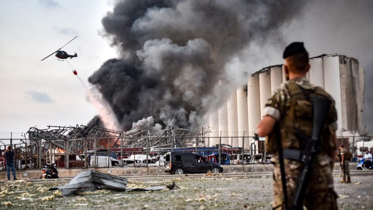 Lebanese army soldiers stand while behind a helicopter puts out a fire at the scene of an explosion at the port of Lebanon's capital Beirut on August 4, 2020. STR / AFP