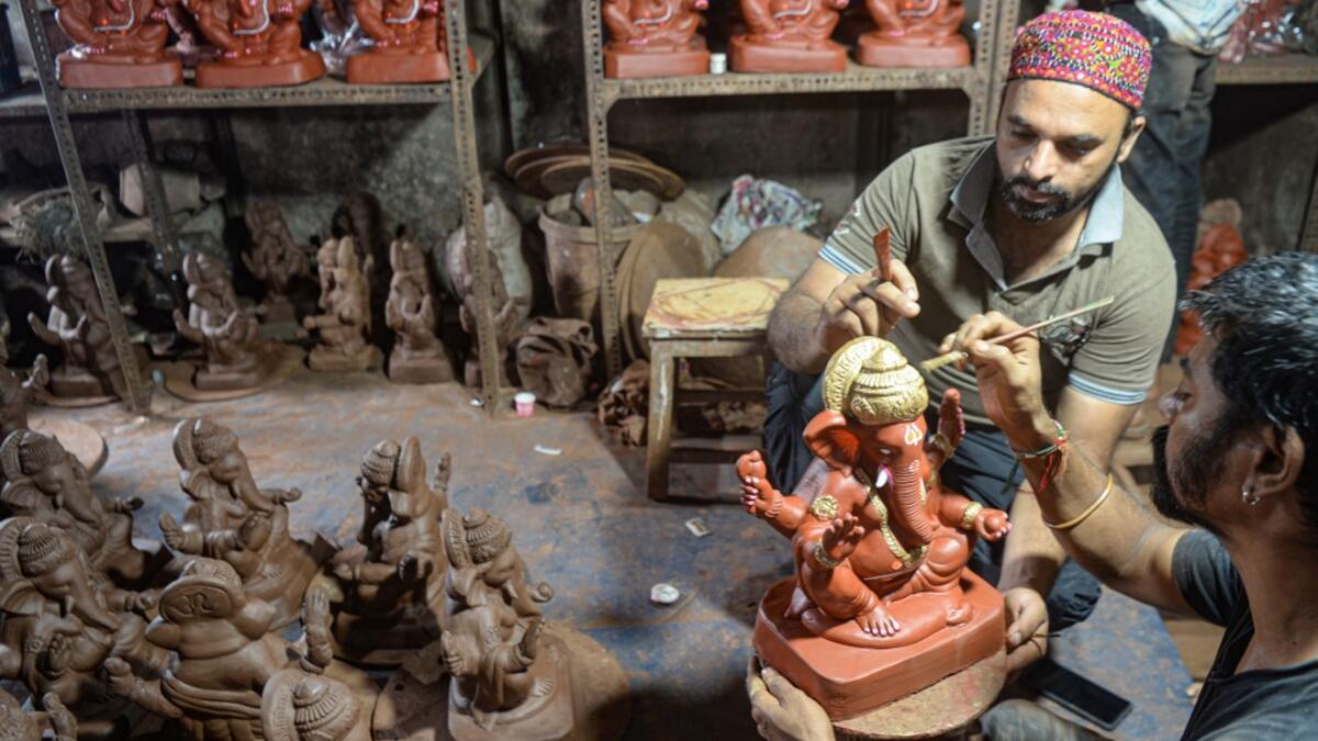In this picture taken on August 11, 2020, Muslim potter Yusuf Zakaria Galwani (L) instructs an artisan as he gives finishing touches to a clay idol of elephant headed Hindu god Ganesha at his workshop at Kumbharwada inside the Dharavi slums in Mumbai. After the coronavirus pandemic clobbered his pottery business, a Muslim artisan from India's largest slum turned to a Hindu god to revive his fortunes by making environmentally-friendly Ganesha idols for an upcoming festival. In Mumbai's Dharavi slum, Galwani