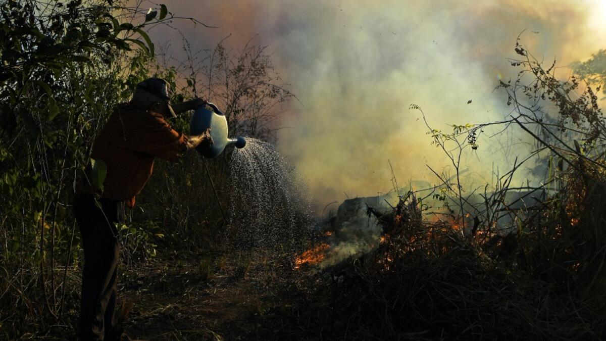 A farmer tries to pour water on an area close to an illegally lit fire in Amazon rainforest reserve, south of Novo Progresso in Para state, Brazil, on August 15, 2020. CARL DE SOUZA / AFP