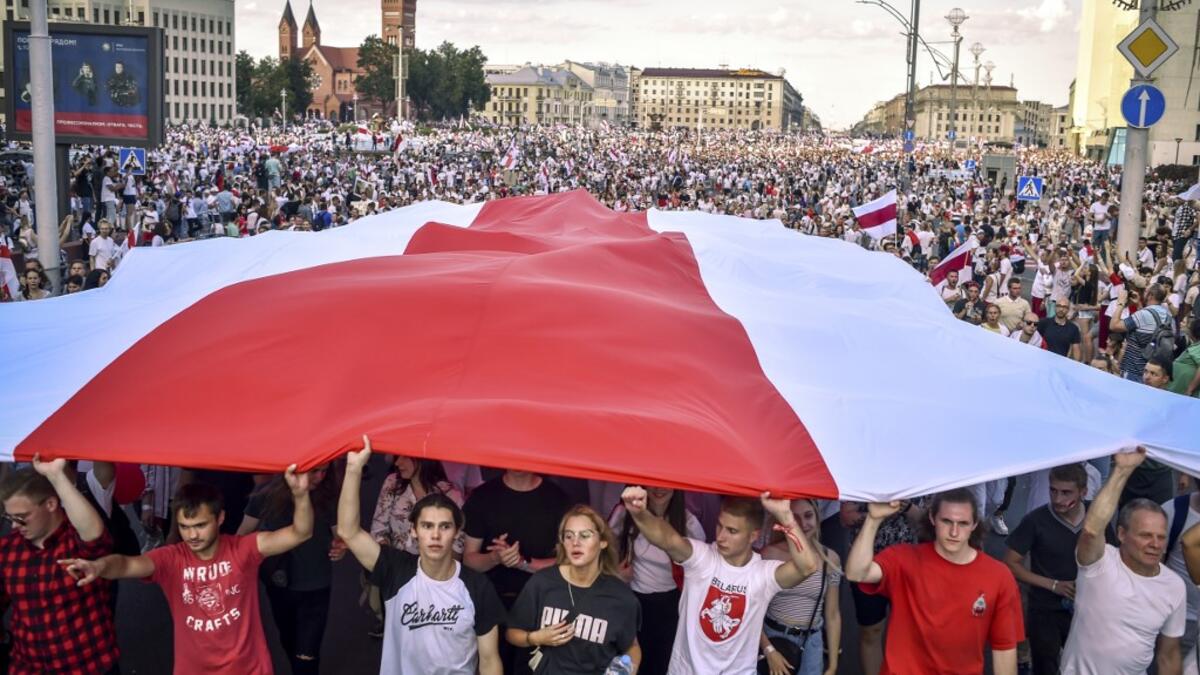 Belarus opposition supporters hold a giant former white-red-white flag of Belarus used in opposition to the government, during a demonstration in central Minsk on August 16, 2020. The Belarusian strongman, who has ruled his ex-Soviet country with an iron grip since 1994, is under increasing pressure from the streets and abroad over his claim to have won re-election on August 9, with 80 percent of the vote. Sergei GAPON / AFP