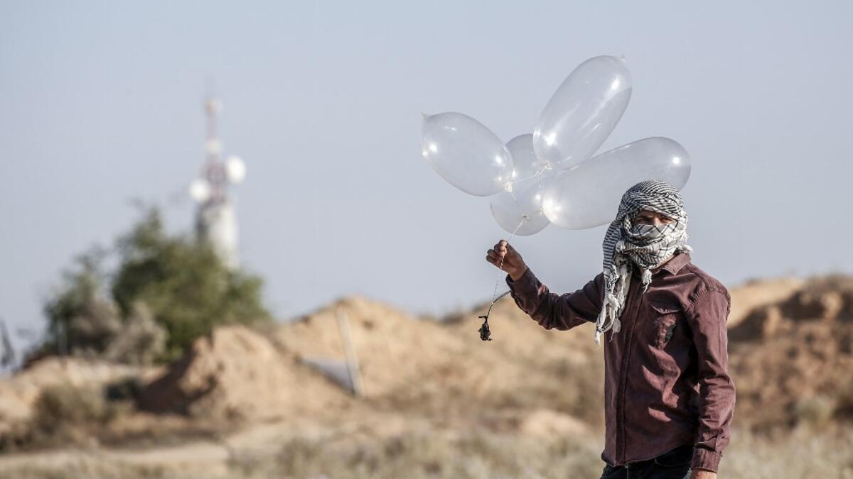 A Palestinian prepares to launch inflated condoms attached with an incendiary device to be directed and flown towards Israel, near Rafah along the border between the Gaza Strip and Israel on August 21, 2020. SAID KHATIB / AFP