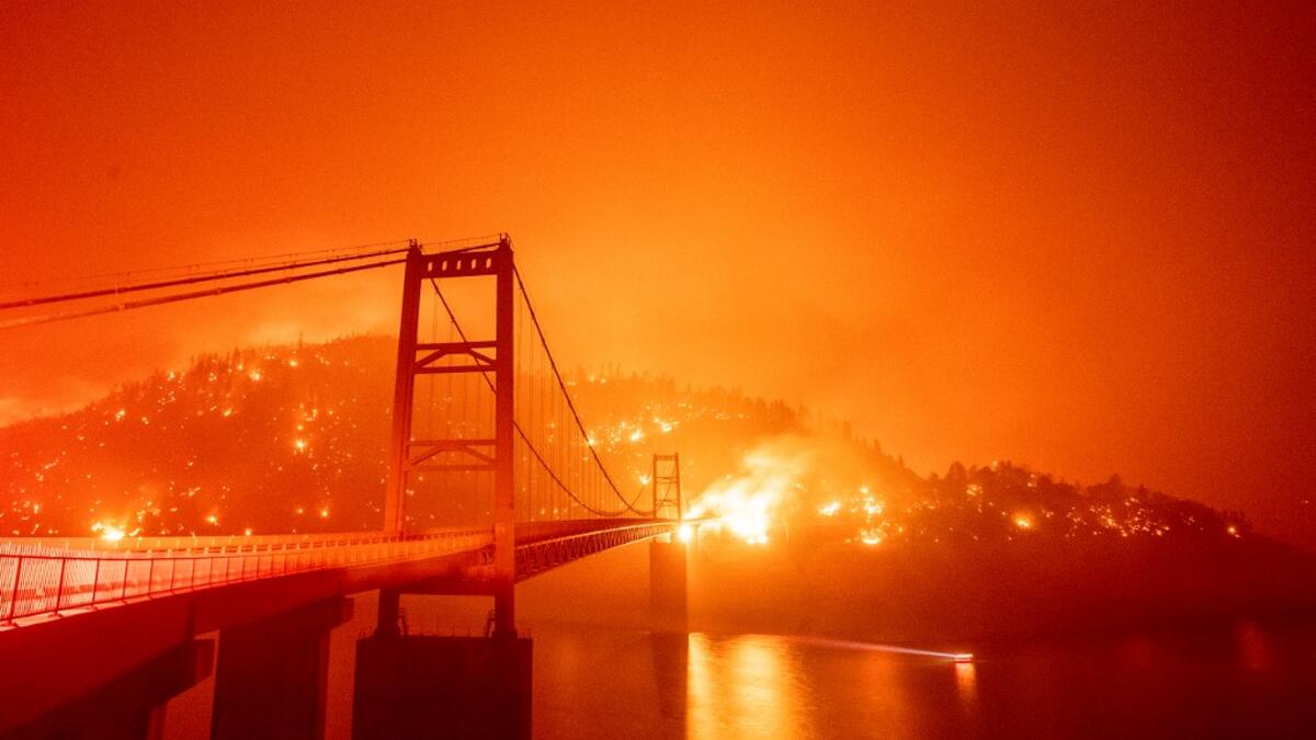 A boat motors by as the Bidwell Bar Bridge is surrounded by fire in Lake Oroville during the Bear fire in Oroville, California on September 9, 2020. Dangerous dry winds whipped up California's record-breaking wildfires and ignited new blazes Tuesday, as hundreds were evacuated by helicopter and tens of thousands were plunged into darkness by power outages across the western United States. JOSH EDELSON / AFP