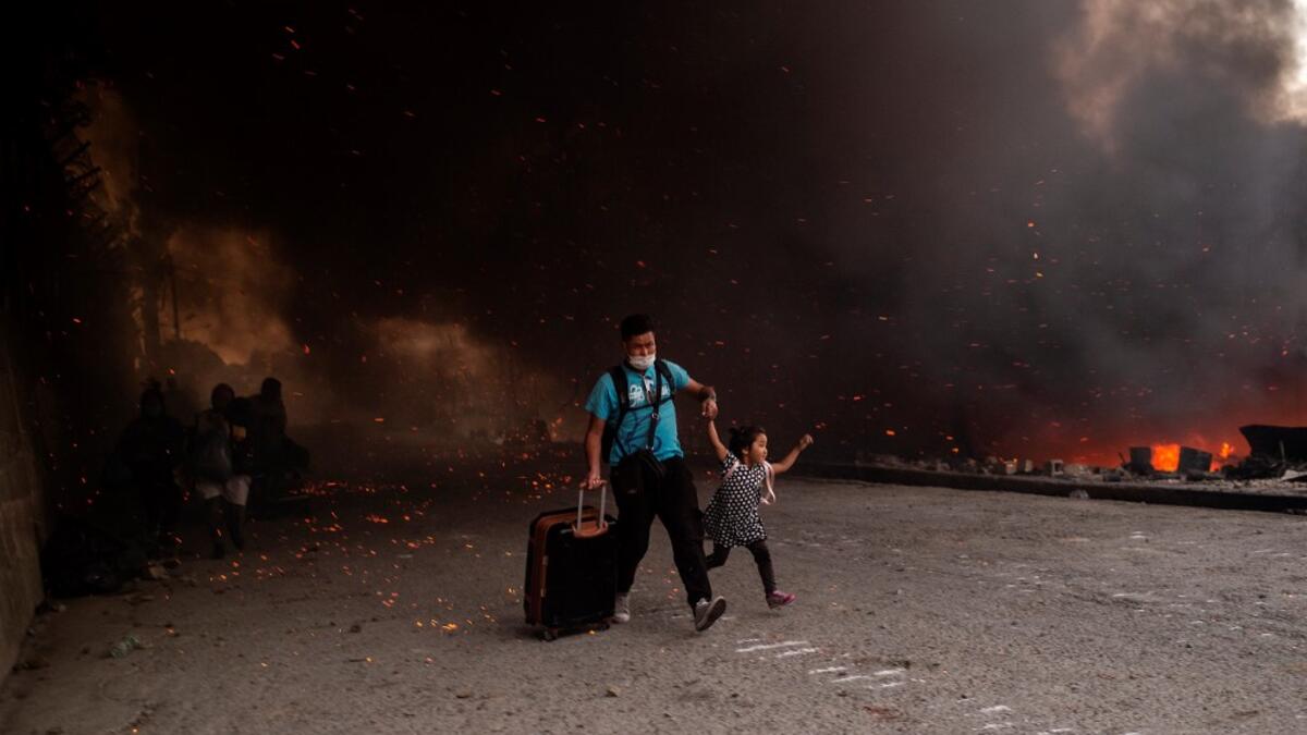 A migrant holds a girl as they flee a fire burning in the Moria camp on the island of Lesbos on September 9, 2020. Thousands of asylum seekers on the Greek island of Lesbos fled for their lives on September 9, 2020 as a huge fire ripped through the camp of Moria, the country's largest and most notorious migrant facility.