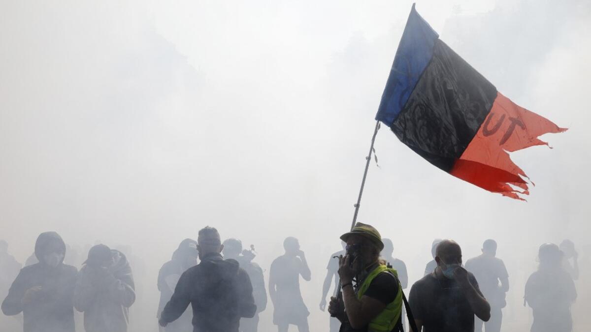 Protesters cover their faces from the tears gas smoke during a demonstration called by the "yellow vest" (gilets jaunes) movement on September 12, 2020 in Paris. GEOFFROY VAN DER HASSELT / AFP