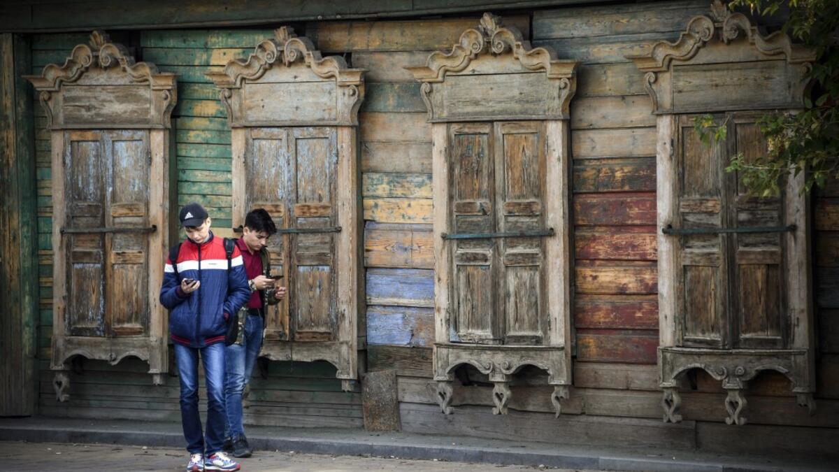 People stand in front of a traditional wooden house in the Siberian city of Tomsk on September 8, 2020. Tomsk is considered to be one of the oldest towns in Siberia founded in 1604. Wooden architecture is one of the symbols of the city of Tomsk, its distinctive feature. Today Tomsk is the only city in Siberia where the background wooden buildings have been preserved, reflecting the manor structure of the city streets. Unfortunately, many wooden houses are not in very good condition and require restoration.